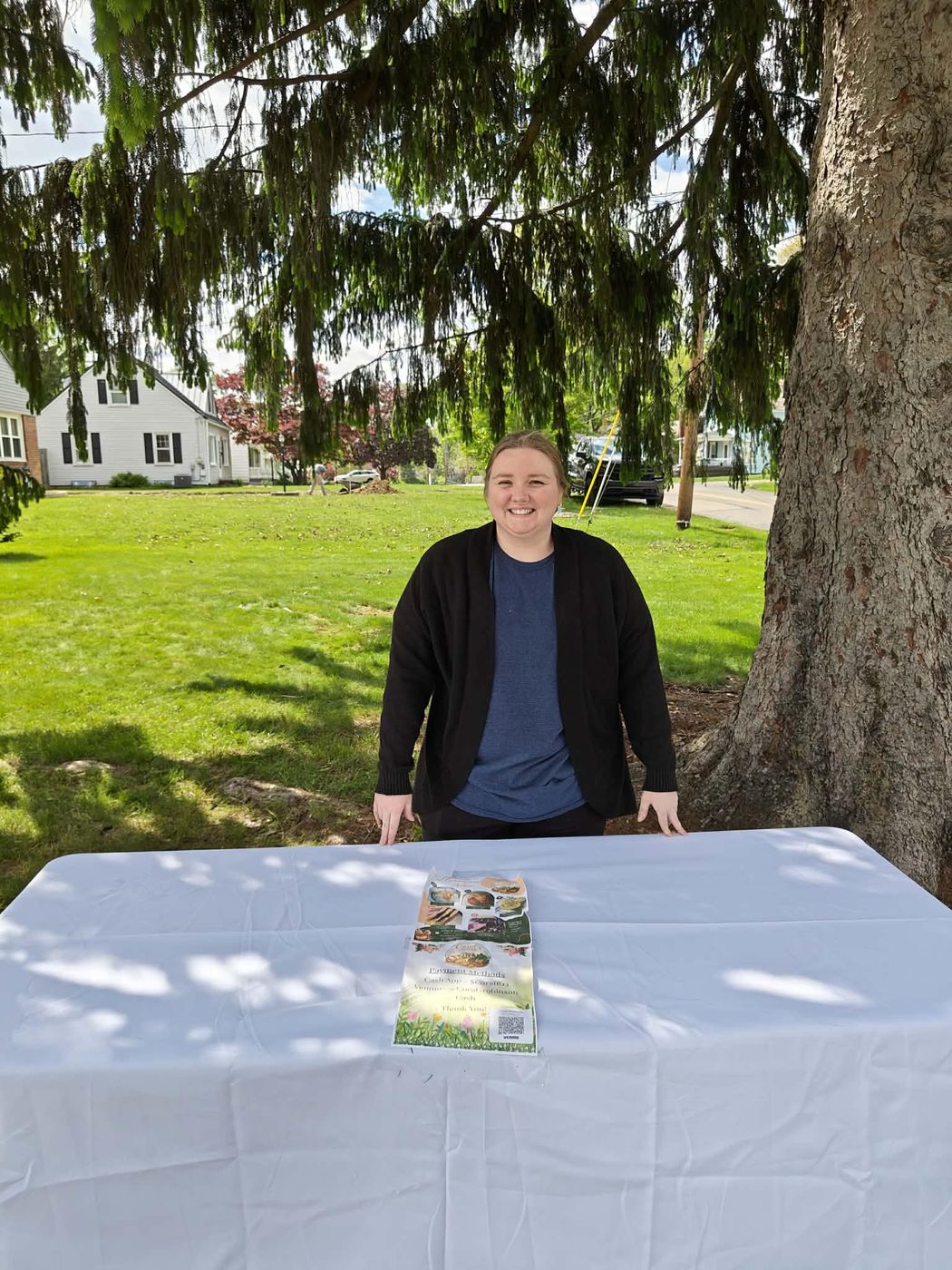 Coral standing at her bakery stand under a tree