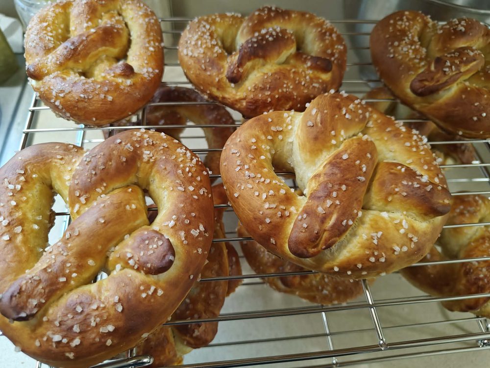 Golden brown sourdough pretzels on a cooling rack with coarse salt